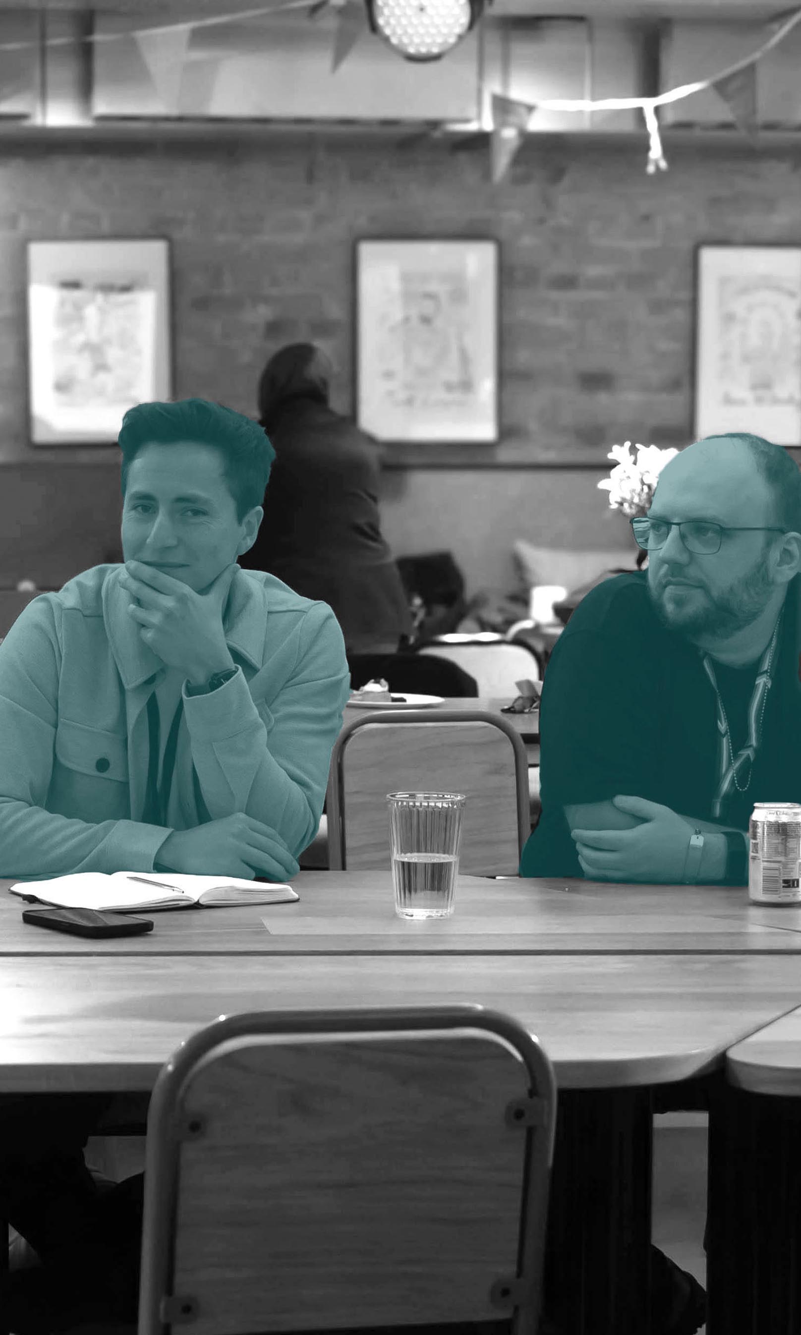 Ein Mann und eine Fraus sitzen am Meetingstisch, die frau schaut in die Kamera, der Mann zur Seite. Bild mit blauen Akzenten.